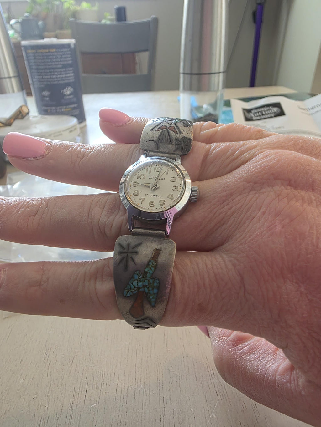 May include: A silver-tone wristwatch with a round white face featuring the text Westclox and 17 Jewels. The band consists of two metal segments decorated with inlaid turquoise and coral stone accents in geometric and bird-like patterns.
